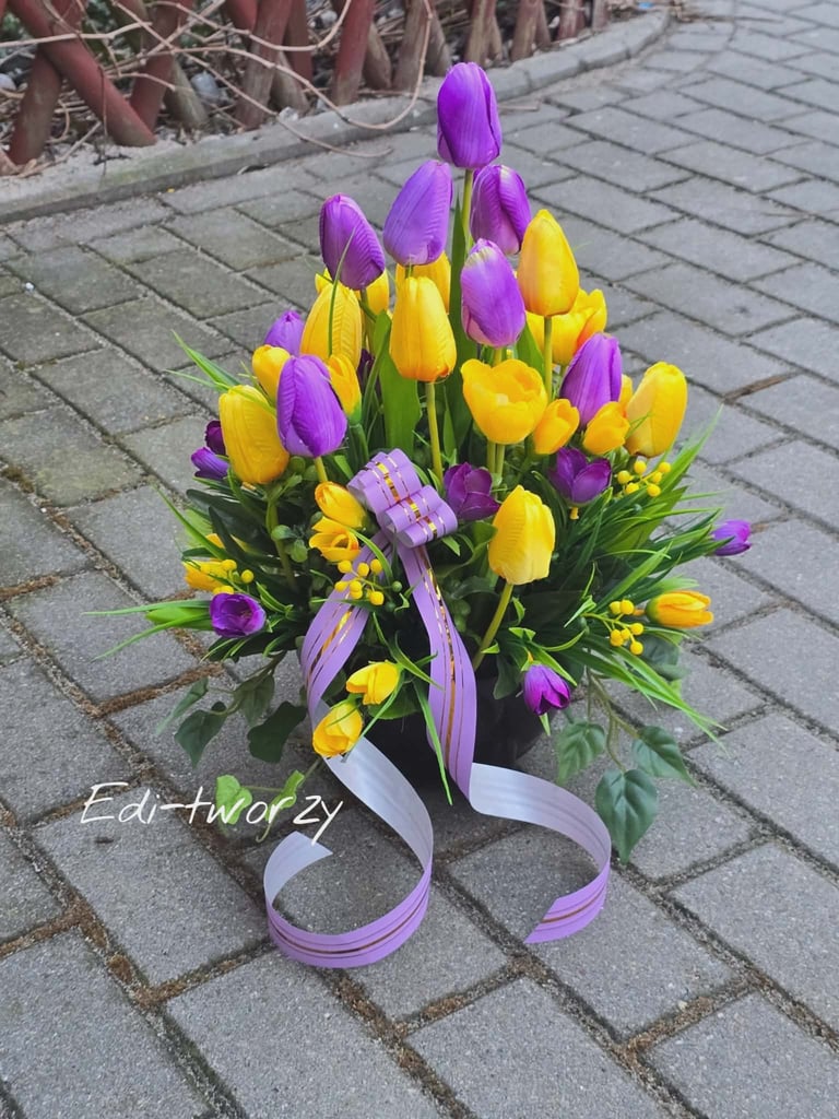 Colorful bouquet of purple and yellow tulips with green foliage tied with lavender ribbons on a paved surface