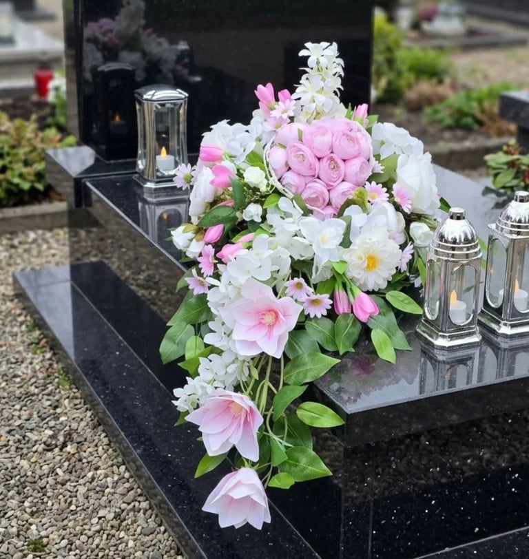 Pink and white flower arrangement with candles on a black gravestone in a cemetery